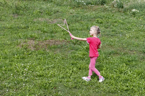 Little girl, blonde, playing in the meadow, and blows a bubble. — Stock Photo, Image