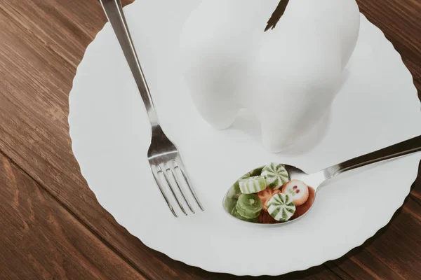 Fondo de madera con un diente grande en un plato. en una cuchara un montón de dulces. hay un enchufe — Foto de Stock