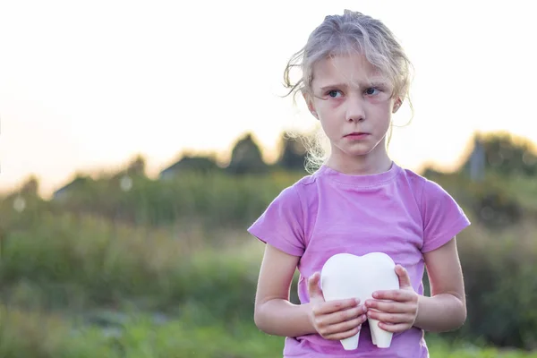 Little girl affliction. holds a large plaster tooth. Shallow depth of field — Stock Photo, Image