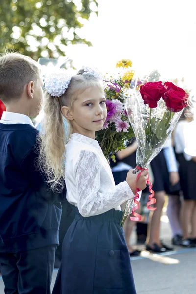 Menina loira segurando flores em suas mãos. o início do ano letivo. primeira chamada . — Fotografia de Stock