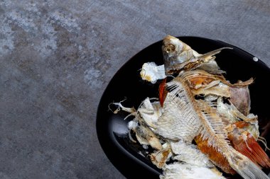 ahşap arka plan. koyu renk bir tabak. yenen balık kemikleri vardır.