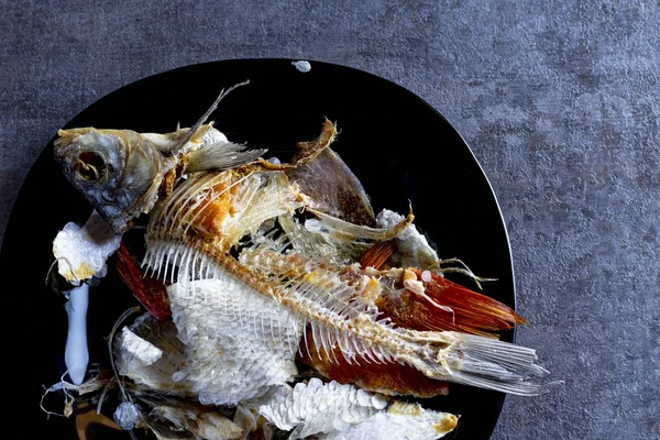 Fond en bois. une assiette de couleur foncée. il y a des os de poissons mangés . — Photo