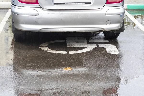 Una macchina d'argento è parcheggiata su un cartello. posto per disabili. primo piano. Sta piovendo. autunno. vergognosamente . — Foto Stock