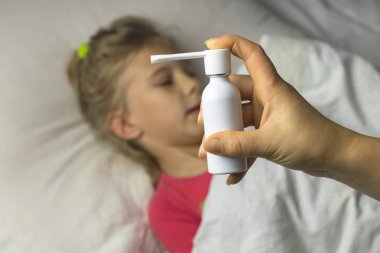 Beyaz saçlı bir kız yatakta uzanıyor. Odaklanamıyor. Anne, astım spreyi kullanarak hastanın boğazına iğne yapıyor. Odaklanıyor..