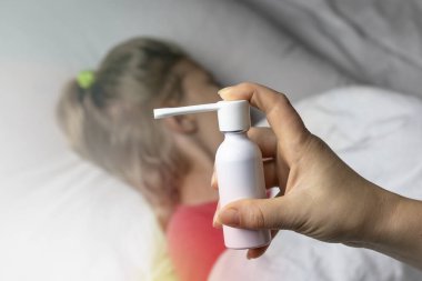 Beyaz saçlı bir kız yatakta uzanıyor. Odaklanamıyor. Anne, astım spreyi kullanarak hastanın boğazına iğne yapıyor. Odaklanıyor..