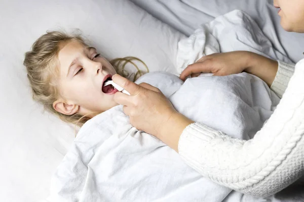 Ένα κορίτσι με άσπρα μαλλιά ξαπλώνει στο κρεβάτι. Η μαμά που χρησιμοποιεί έναν εισπνευστήρα κάνει μια ένεση στο λαιμό ενός ασθενούς. — Φωτογραφία Αρχείου