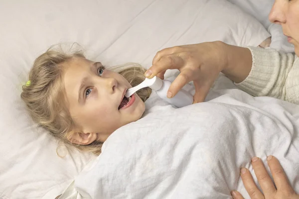 Une fille aux cheveux blancs est couchée. maman utilisant un inhalateur fait une injection dans la gorge d'un patient . — Photo