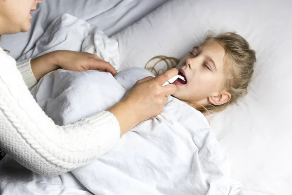 A girl with white hair lies in bed. mom using an inhaler makes an injection in the throat of a patient. — Stock Photo, Image