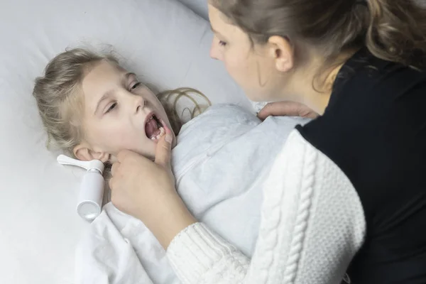 흰머리를 한 소녀가 침대에 누워 있다. 엄마가 흡입기를 사용하여 환자의 목구멍에 주사를 놓는 모습. — 스톡 사진