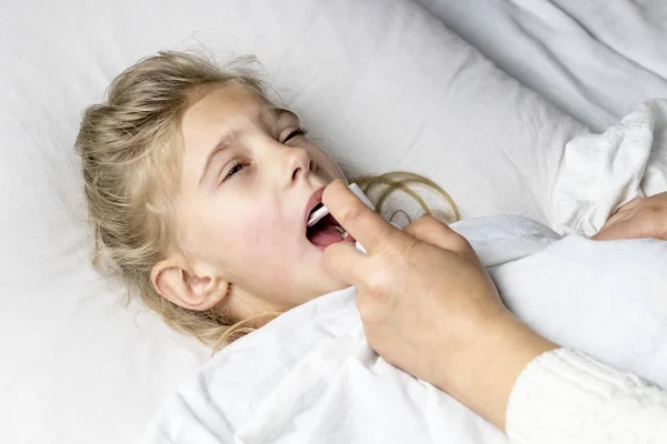 Une fille aux cheveux blancs est couchée. maman utilisant un inhalateur fait une injection dans la gorge d'un patient . — Photo