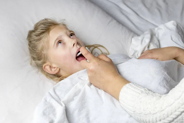 Une fille aux cheveux blancs est couchée. maman utilisant un inhalateur fait une injection dans la gorge d'un patient . — Photo