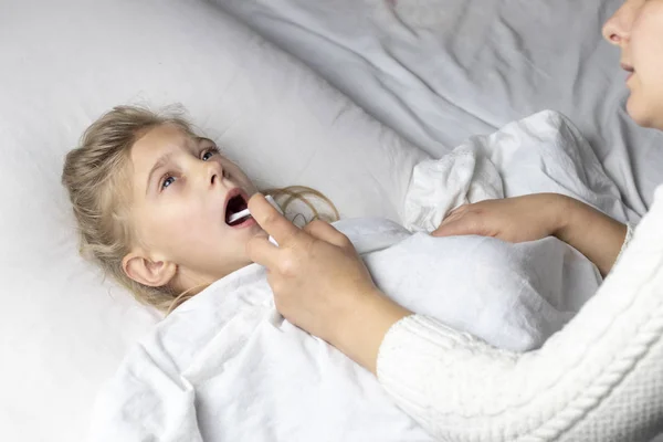 Seorang gadis dengan rambut putih berbaring di tempat tidur. ibu menggunakan inhaler membuat suntikan di tenggorokan pasien . — Stok Foto