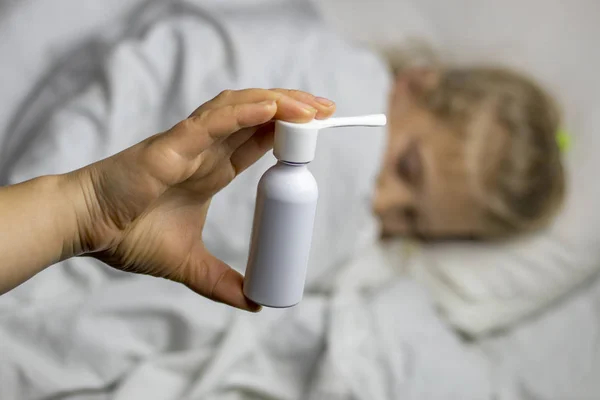 Ein Mädchen mit weißem Haar liegt im Bett, sie ist unscharf. Mutter mit Inhalator spritzt dem Patienten eine Spritze in den Rachen, sie steht im Fokus. — Stockfoto