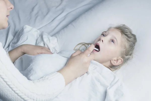흰머리를 한 소녀가 침대에 누워 있다. 엄마가 흡입기를 사용하여 환자의 목구멍에 주사를 놓는 모습. — 스톡 사진