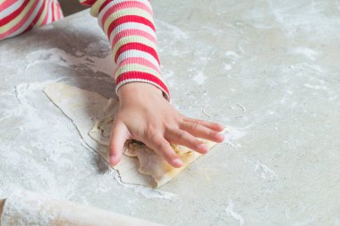 Ev mutfağı. Masanın üzerinde pişirmek için bir hamur var. Bir çocuk içine bir form sıkıştırıyor..