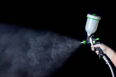 Lastik eldivendeki bir el mekanik bir atomizer tutar. Tetiği tutuyor, püskürtüyor. Siyah arkaplan.