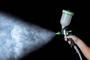 Lastik eldivendeki bir el mekanik bir atomizer tutar. Tetiği tutuyor, püskürtüyor. Siyah arkaplan.