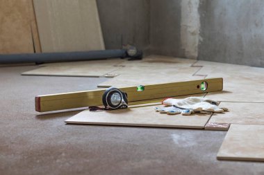 Banyo. Tadilat yapılıyor. Seramik fayanslar yere konur. Seviye, mezura ve eldivenlere odaklan. Yakın plan.