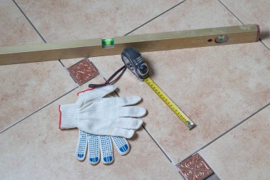 Banyo. Tadilat yapılıyor. Seramik fayanslar yere konur. Seviye, mezura ve eldivenlere odaklan. Yakın plan.