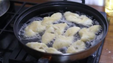 Mutfak. Kızartma tavasında sıcak ayçiçeği yağı var. Elleriyle çiğ hamur koyuyorlar. İçi boşaltılmış.