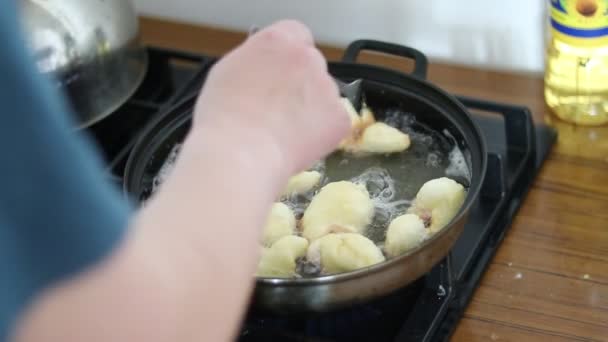 Cuisine. Dans une poêle, il y a de l'huile de tournesol chaude. Ils y ont mis de la pâte crue avec leurs mains. Elle est drainée. — Video