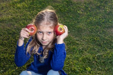 Yumuşak odaklanma. Gün ışığı. Beyaz saçlı bir kız elinde iki kırmızı elma tutuyor. Güneş batıyor.
