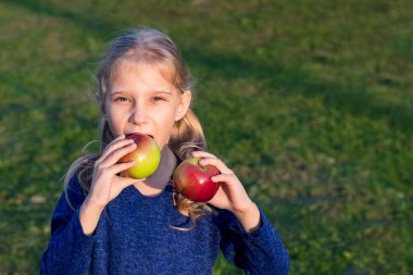 Yumuşak odaklanma. Gün ışığı. Beyaz saçlı bir kız elinde iki kırmızı elma tutuyor. Güneş batıyor.