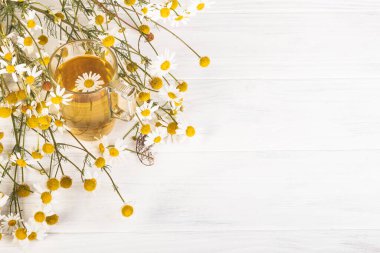 Geçmişe dönük beyaz ahşap arka plan. Üzerinde papatya çayının demlendiği cam bir bardak var. Uzayı kopyala metin