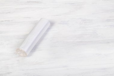 Ahşap arka plan yapay olarak yaşlandırılmış. Üzerinde bir rulo şeffaf polietilen poşet var. Çevre kirliliği. Geri dönüşüm