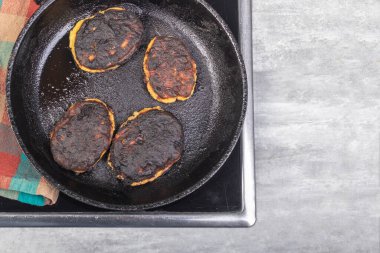 Elektrikli soba. İndüksiyon. Üzerinde yemek olan bir kızartma tavası var. Yemekler yanmış.