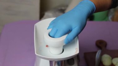 Elektrikli beyaz et öğütücüsü. Kıyma dilimlenmiş eti metal bir kaseye koyar. Mavi eldivenli bir insan eli her şeyi düzeltir.