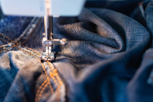 Repair jeans on the sewing machine. View of the fabric, needle and thread. Illumination from the built-in incandescent lamp. Jeans are a type of trousers, typically made from denim or dungaree cloth