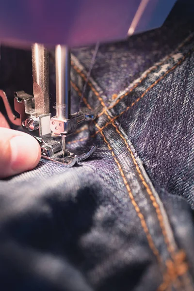 Repair jeans on the sewing machine. View of the fabric, needle and thread. Illumination from the built-in incandescent lamp. Jeans are a type of trousers, typically made from denim or dungaree cloth