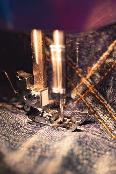 Repair jeans on the sewing machine. View of the fabric, needle and thread.  Real motion blur. Lit by the built-in incandescent lamp. Jeans are a type of trousers, typically made from denim