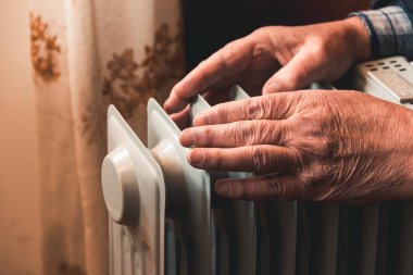 İhtiyar bir adamın elleri üzerinde bir elektrikli ısıtıcı ısıtıyor. Sezon içinde Merkezi Isıtma gecikir, böylece insanlar ek satın almak zorunda rağmen ısıtıcılar evleri devam sıcak artan elektrik faturalarını.