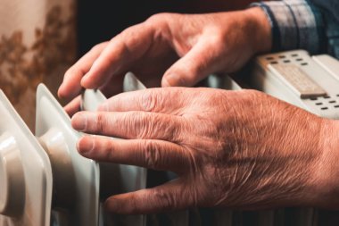 İhtiyar bir adamın elleri üzerinde bir elektrikli ısıtıcı ısıtıyor. Sezon içinde Merkezi Isıtma gecikir, böylece insanlar ek satın almak zorunda rağmen ısıtıcılar evleri devam sıcak artan elektrik faturalarını.