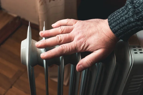 Bir adam eliyle bir elektrikli yağ ısıtıcı sıcaklığını denetler. Sezon içinde Merkezi Isıtma her zaman çalışmaz. Ek ısıtıcılar evin sıcak tutmak gerekiyordu. Elektrik faturalarını arttı