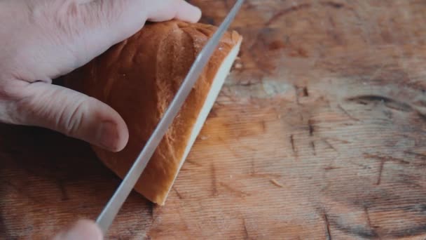 男性の手は 木製キッチンまな板の上鋼ナイフで白パンのパンをカットします 朝食用のパンを提供しています 上からの眺め フラットが横たわっていた クローズ アップ — ストック動画