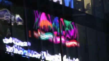 Led neon reklam bir gökdelenin cam Windows yansımaları. Gece şehir. İnsanlar geçip