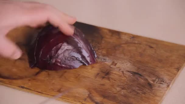 Uma cabeça de repolho vermelho é cortada com uma faca de aço na mesa de madeira — Vídeo de Stock