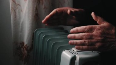 Kıdemli yaşlı adam ellerini elektrikli ısıtıcı ısıtıyor. Sezon içinde Merkezi Isıtma gecikir, böylece insanlar ek satın almak zorunda rağmen ısıtıcılar evleri devam sıcak artan elektrik faturalarını
