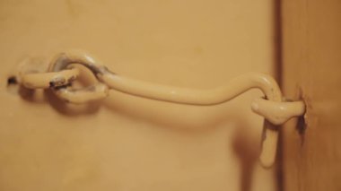 Erkek el kapı kanca asansörleri ve kapıyı açar. Akşamları akkor aydınlatma. Ahşap kapı boyalı bej var. Karanlık kapı. İlkel basit kapı kilidi