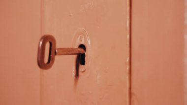 Ahşap kapı anahtar deliği demir anahtar. Erkek el anahtarı kapatır ve kapıyı açar. Akşamları akkor aydınlatma. Ahşap kapı bej boya ile boyanmış. Karanlık kapı. Basit kapı kilidi