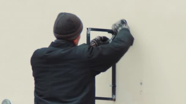 Работник в шляпе на лестнице крепится металлическая конструкция — стоковое видео