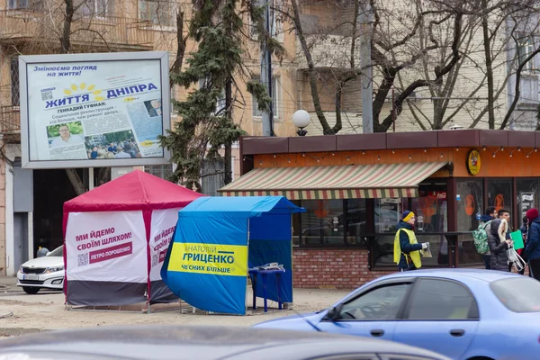 Dnipro, Ukraina - 4 mars 2019: Gatan arrangören distribuerar tidningar och kampanjmaterial nära tält reklam kandidat för President i Ukraina, Anatoly Gritsenko och Petro Poroshenko — Stockfoto