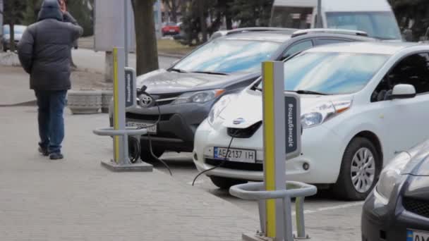 Lidé chodí blízko zaparkované elektrické vozidlo připojeno k nabíječce — Stock video