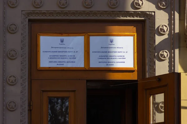 DNIPRO, UKRAINE - 31 mars 2019 : Entrée du bureau de vote dans le bâtiment universitaire. Élection du Président de l'Ukraine. Drapeau ukrainien flottant près de la porte — Photo