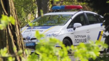 Devriye polis arabası şehir parkında ağaçların arkasına park edilmiş.