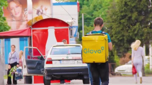 Glover con una mochila amarilla con Glovo! logo está caminando — Vídeos de Stock