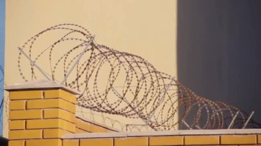 Batan güneşin ışınlarıyla aydınlatılan bir tuğla çitüzerinde dikenli tel.